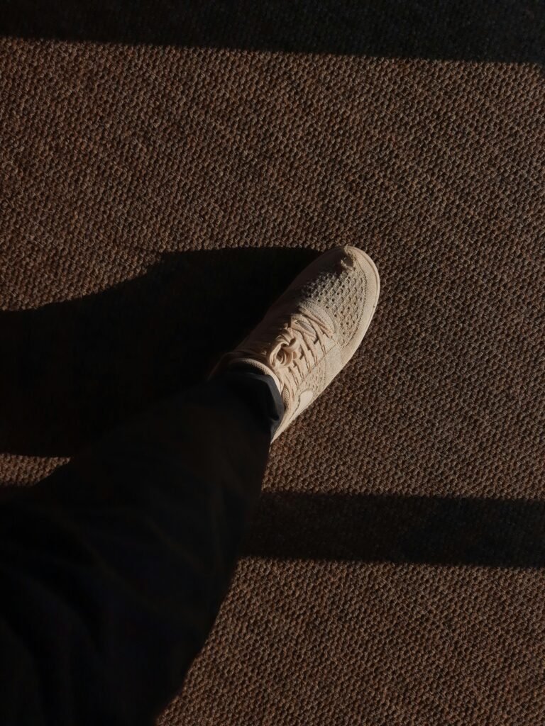 pexels-photo-17153658-17153658 A white sneaker steps on a textured carpet casting a long shadow.